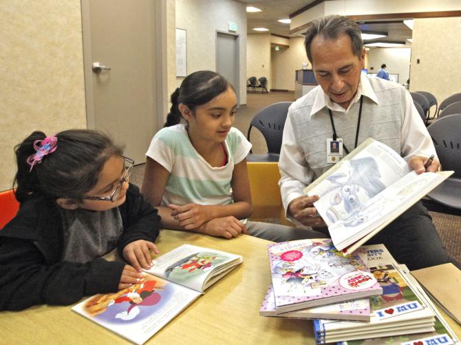 Administrator Richard Castro shares some of his favorite books with Giovanna Agular and Valaria Ruiz-Escalante at Eastside. Free books are often given out to kids during visits to the community health centers (Ken Papaleo)