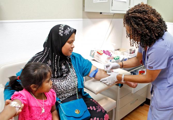 Gennet Gameda, a healthcare partner at Lowry Family Health Center, prepares to take blood from Ai Str while her daughter, Joma Bi, looks on (Ken Papaleo)